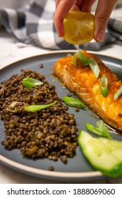 Hand Squeezes Lemon Juice On A Baked Honey-soy Glazed Salmon Fillet Served With Black Beluga Lentils, Cucumber And Green Onions. Healthy Fresh Salmon Steak For Lunch Or Dinner. Side View