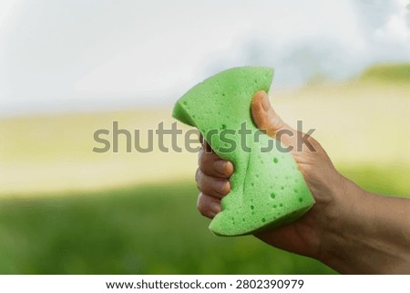 Hand squeezing a green cleaning sponge with a blurred nature background