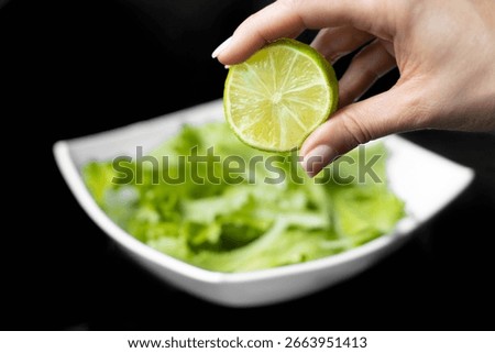 Hand squeezing half of a fresh lime on a black background.