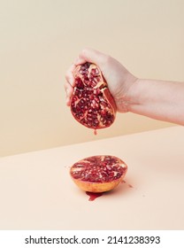 hand squeezing half a juicy pomegranate, drop of ruby-colored juice splashing down, on a diagonal two-color background
