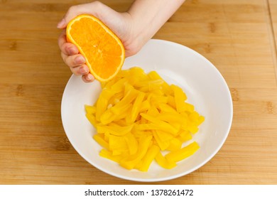 Hand squeezing half orange on a bowl with stripped jackfruit.