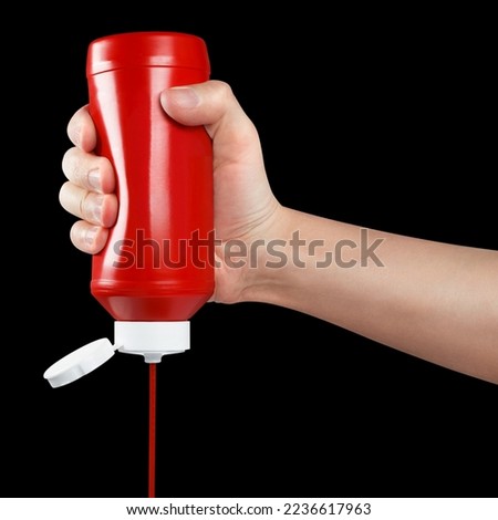 Hand squeezing ketchup out of a plastic bottle, isolated on black background