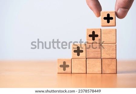 Hand stacking increasing of plus sign on wooden block cube for value added concept.