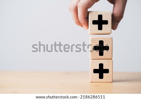 Hand stacking plus sign which print screen on wooden cube block for addition and positive mindset thinking concept.