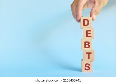 Hand stacking word debts in wooden blocks. Growing financial debt, pile up, accumulation, stockpile and increase concept.