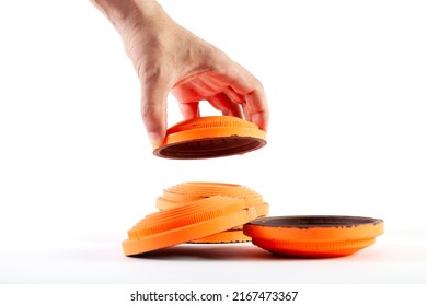 A Hand Stacks Round Orange Target Cymbals In A Stack On A White Background. Two Targets Lie Nearby. Close-up

