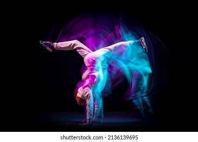 Hand stand. One energy young flexible sportive man dancing hip-hop or breakdance in white outfit on dark background in mixed blue neon light. Concept of sport, art, action, moves, youth culture.
