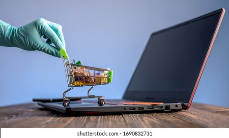 A hand in a sterile medical glove holds a shopping cart with a credit card for online purchases. Concept of internet purchasing important life support products during the coronavirus pandemic