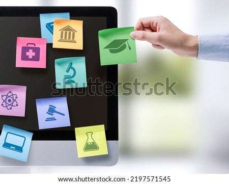 Hand sticking notes with educational subjects icons on a computer screen, online learning concept