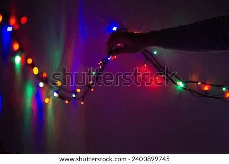 Hand sticking putting christmas string lights with tape on a wall in a dark room. Christmas home decoration concept. decorating the wall with christmas lights close up
