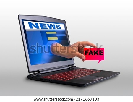 A hand sticks out of the laptop screen and holds a sign that says fake, a concept of propaganda and advertising on the Internet. creative composition,