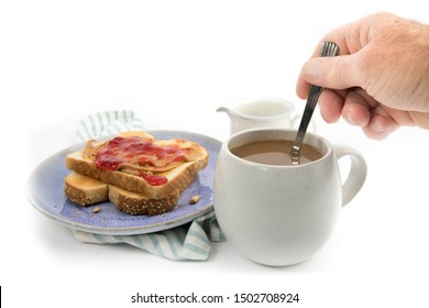 A Hand Stirring Cream Into A Cup Of Coffee With A Peanut Butter And Jam On Toast Isolated On White