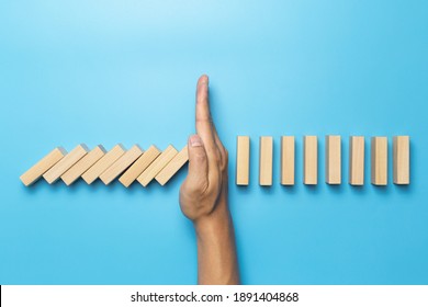 Hand stopping the domino effect on wooden table blue. Business Risk management concept. Business strategy