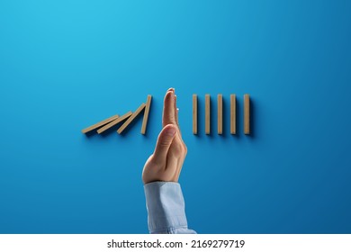 A Hand Stops The Tipping Over Of Wooden Dominoes. Concept Of Containment Of Problems.