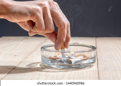 Hand stubbed out cigarette in a transparent ashtray on wooden table