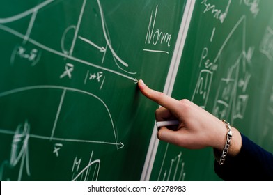 Hand of a student pointing at green chalkboard with normal distribution on it