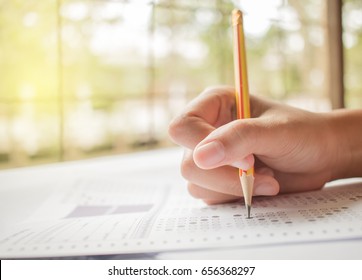 hand student testing in exercise and taking fill in exam carbon paper computer sheet with pencil at school test room, education concept