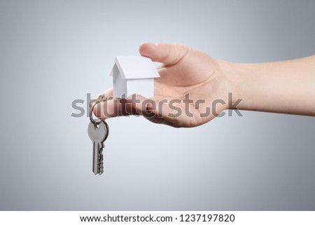 Hand suggesting a key and a small white house on grey background