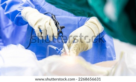 Hand of the Surgeon holds surgical instrument inside operating room in hospital.Doctor in blue uniform did minimal invasive endoscopic keyhole spine disc surgery technology.People work with light
