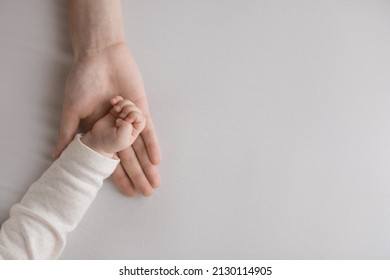 Hand of sweet few month baby resting in mothers palm. Mom holding, touching tiny arm of little sleepy daughter, son. Kid lying on bed with white sheet. Close up, cropped shot. Motherhood concept - Shutterstock ID 2130114905