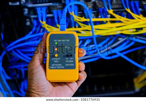 hand of system administrator or\
technician with tester tool for test network cables connected to\
patch panel of network gigabit switch in network data\
center