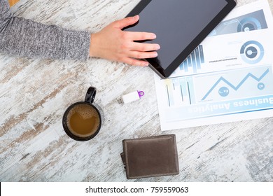 A womanâ??s hand at a table useing a tablet.