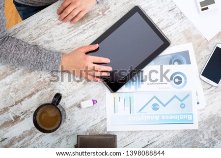 A woman’s hand at a table useing a tablet.