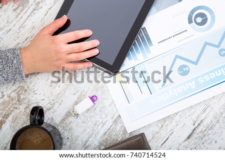 A womanâ??s hand at a table useing a tablet.