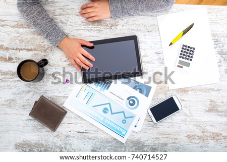 A womanâ??s hand at a table useing a tablet.