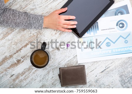 A womanâ??s hand at a table useing a tablet.