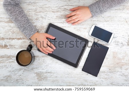 A womanâ??s hand at a table useing a tablet.