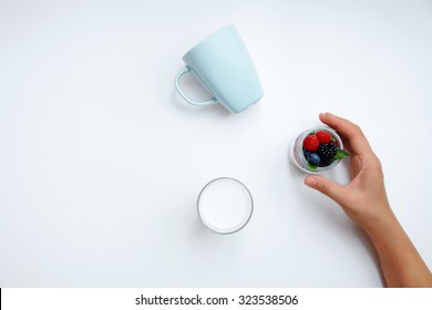 Hand Takes Jar Filled With Tasty Berries Wtih Mint Leaves; Glass Of Milk Top View