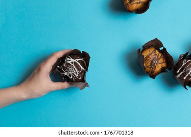 hand takes a muffin, cakes on a blue bright background