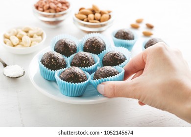 Hand Takes No Bake Brownie Energy Bite From White Plate. Concept Of Healthy Gluten-free Vegan Snacks.