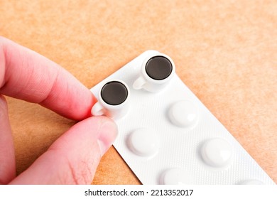 Hand Takes A Teeny-tiny Coffee Cup Placed On A Tablets Blister Isolated. Caffeine Pills Dosage Concept.