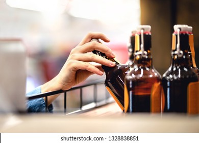 Hand Taking Bottle Of Beer From Shelf In Alcohol And Liquor Store. Customer Buying Cider Or Supermarket Staff Filling And Stocking Shelves. Retail Worker Working. Woman Choosing Lager Or Pale Ale