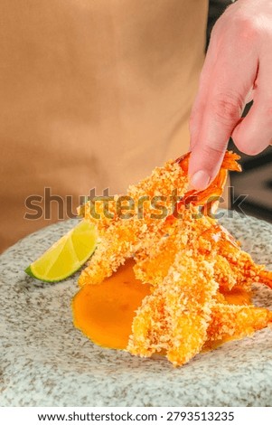 Hand taking crispy breaded shrimp served with mango sauce and lime. Gourmet seafood appetizer with interactive dining concept.