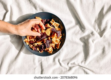 Hand taking crunchy vegetable chips from a plate on the table with linen tablecloth. Veggie snack. Alternative healthy eating. Proper nutrition. Dehydrated vegetables - Shutterstock ID 2078368096