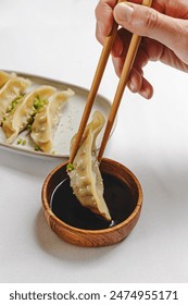 Hand taking gyoza dumpling from the plate with chopsticks, close-up view