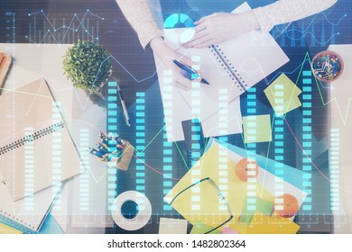 Hand taking notes in notepad. Forex chart holograms in front. Concept of research. Double exposure