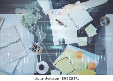 Hand taking notes in notepad. Forex chart holograms in front. Concept of research. Double exposure