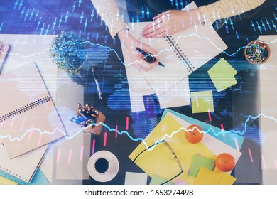 Hand taking notes in notepad. Forex chart holograms in front. Concept of research. Double exposure