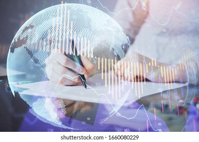 Hand taking notes in notepad. Forex chart holograms in front. Concept of research. Multi exposure