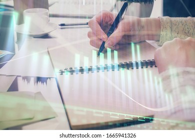 Hand taking notes in notepad. Forex chart holograms in front. Concept of research. Double exposure