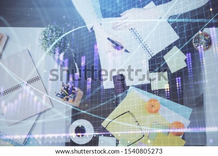 Hand taking notes in notepad. Forex chart holograms in front. Concept of research. Double exposure