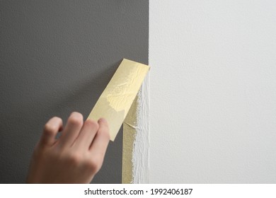 Hand taking off masking tape from the wall after painting. Home renovation tricks and minimalistic style. - Shutterstock ID 1992406187