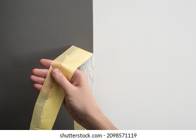Hand taking off masking tape from the wall. Perfect sharp line between gray and white parts. Home renovation ideas. - Shutterstock ID 2098571119
