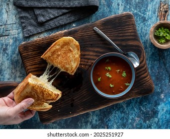 Hand taking one half of a grilled cheese sandwich and a bowl of tomato soup. Soup and sandwich combo concept. - Powered by Shutterstock