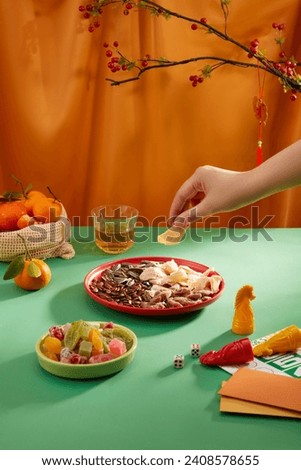 A hand is taking a piece of jam from a plate of nuts and jam on the table. A set of seahorses, a basket of tangerines and a tray of sweets on a green background. Tet concept.