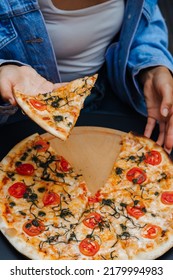 Hand Taking A Slice Of Pizza From Table. Big Pizza Without One Piece.